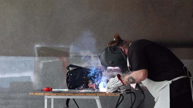 Fabricator in safety gear assembling metal part using electrode holder during welding process