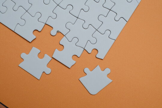 White jigsaw puzzle with two missing pieces separated on an orange background. Concept for problem solving, team collaboration, finding solutions, business integration, and strategic thinking