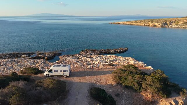 Captivating views of Paros Islands coastline during sunset. A peaceful fishing boat rests by the shore, while travelers explore the tranquil beaches nearby with a camper van