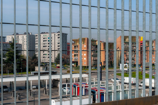 Moderni edifici residenziali visti attraverso una recinzione metallica con sbarre verticali. Ambientazione urbana. Il cielo &egrave; limpido. 