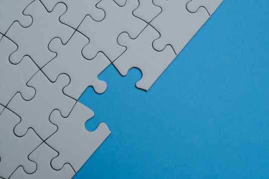 White jigsaw puzzle pieces half-assembled on a vibrant blue background with copy space. Represents business strategy, teamwork, finding solutions, problem-solving, and incomplete tasks