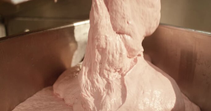 Pink meat paste moves along a blue conveyor in a food plant