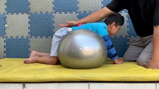 Pediatric physical therapy session with therapist assisting child on exercise ball for sensory integration and motor development