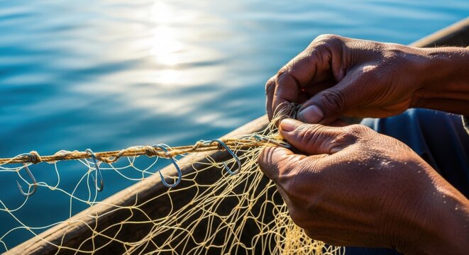 Fishing net repair with focused hands tying knots on fishing net while sitting in boat near shimmering water surface. Fishing net repair demonstrates traditional craftsmanship in aquatic setting.