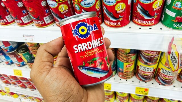 Malaysia Kuala Terengganu 18 July 2026: Hands holding canned sardines displayed on a supermarket shelf. Retail grocery product packaging arranged neatly in a supermarket, showcasing canned seafood pro