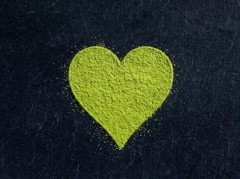 Top-down studio shot of green matcha powder formed into a perfect heart shape on a textured dark slate surface. Creative concept for matcha lovers.