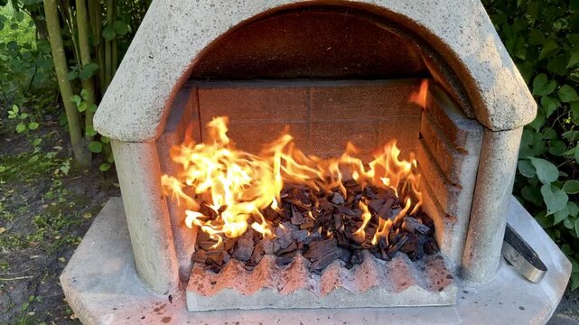 Fire Burning in Stone Garden Fireplace with Green Hedge Behind