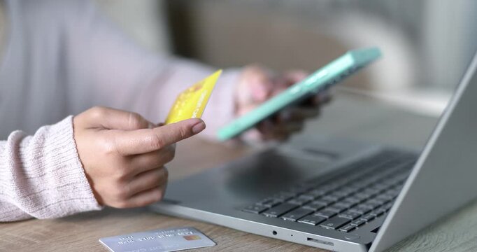 Close-up of a woman holding a credit card while using a laptop for online payment. e-commerce, secure digital transaction, online shopping, fintech, and cashless payment