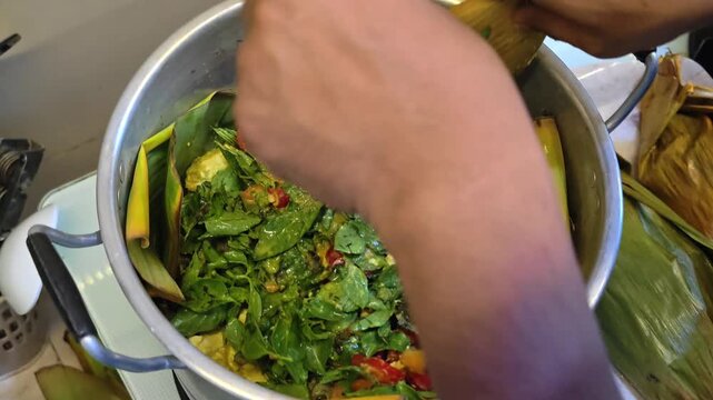 An overhead view showing someone arranging packages of spicy, traditionally prepared steamed fish&mdash;wrapped in banana leaves&mdash;into a large metal pot. 4K