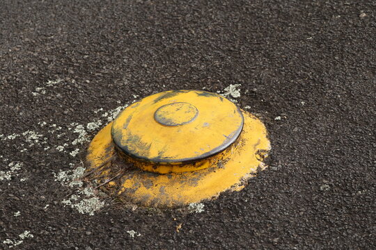 Yellow Metal Road Stud Embedded in Dark Asphalt Surface