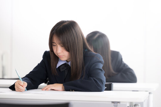 綺麗な新緑背景の教室で真剣にテストに取り組む日本人女子高校生複数　受験、定期テスト、模試の学生