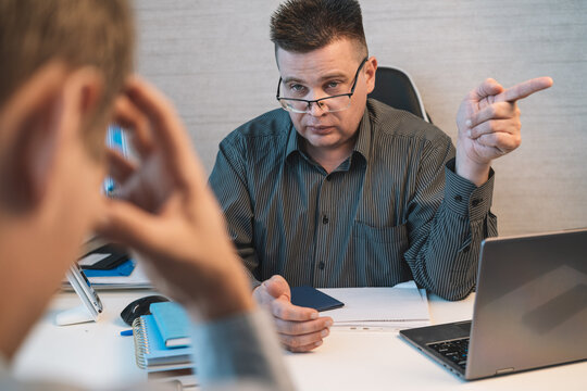 Strict businessman reprimanding an employee during an office meeting, pointing toward the exit while discussing poor performance, dismissal, and workplace discipline.