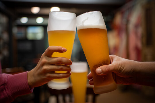 Friends clinking glasses of draft beer in pub. Close-up toast with frosty beer glasses, celebration, social gathering, nightlife, brewery, restaurant and leisure concept.