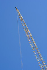 Low angle view of a white steel lattice boom of a construction crane stretching diagonally into a clear vibrant blue sky © nahhan