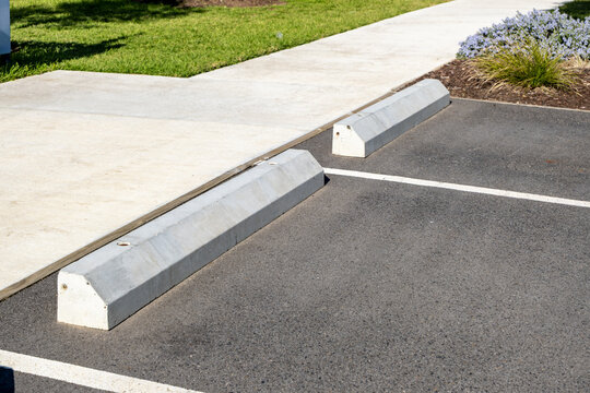 Precast concrete wheel stops installed in empty asphalt parking spaces in Australia.&nbsp;The parking bays are marked with&nbsp;white painted lines and sit adjacent to a&nbsp;pedestrian footpath.