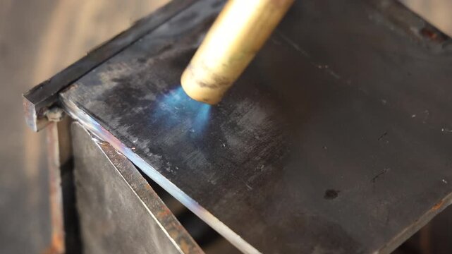 Close up of a gas torch heating a steel metal plate with bright blue flame