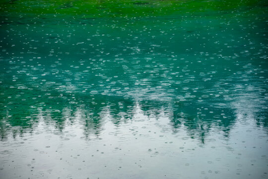 Raindrops creating ripples on the emerald waters of Lake Carezza, Italy. A peaceful nature background captured in the Dolomites