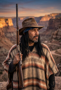 Man in cowboy hat with rifle at sunset in a desert canyon