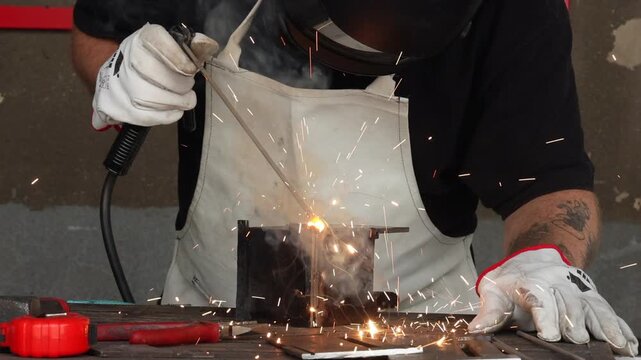 Selective focus on welder hands holding electrode rod with sparks flying in a garage