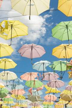 Vertical image featuring numerous multicolored umbrellas suspended above a street. Low angle view with a blue sky and white clouds in the background