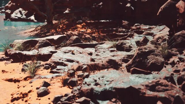 A rocky area is shown with sandy ground and patches of grass. A river is visible in the distance. The sunlight shines on the rocks and water creating a bright view.