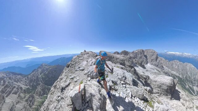 Hiker traversing an exposed alpine ledge with panoramic views toward Paganella on Via Ferrata Bocchette Alte