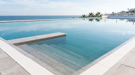 Fototapeta premium Infinity pool with submerged steps overlooking a calm sea and white villas
