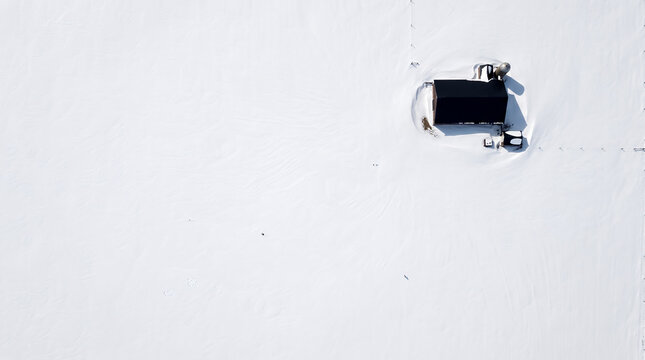 Overhead view of a small dark cabin alone on an untouched snowfield
