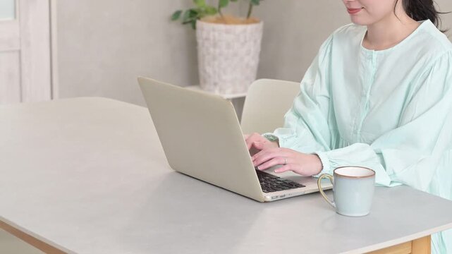 リビングでノートパソコンを使って作業する30代女性の手元