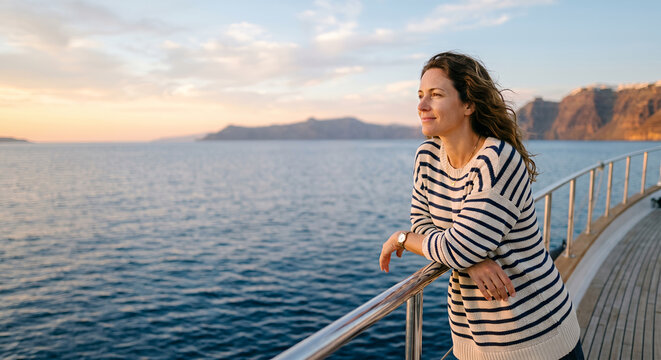 Woman leaning on boat deck railing at sea sunset