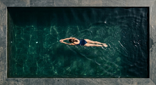 Woman swimming a lap in sunlit dark green pool