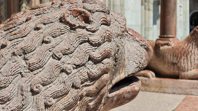 close-up of weathered stone lion statue with its mouth open. Serving as pillar base outside historic San Geminiano cathedral. Highlighting rich Italian architectural heritage and town hall bell tower