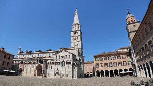 Modena Cathedral, a UNESCO World Heritage site, displaying its Romanesque architecture and the Ghirlandina Tower against clear blue sky, located on the historic Piazza Grandey of Modena city in Italy