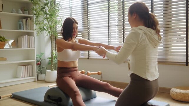Pilates instructor assisting woman with hip stretch exercise on mat, side profile view during guided flexibility session, professional coaching in bright home studio wellness scene