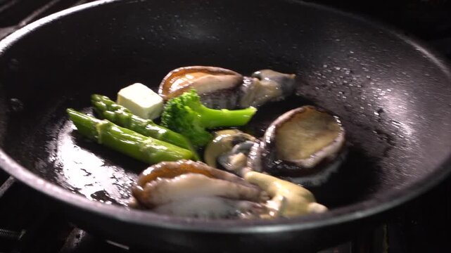 Placing a frying pan with abalone and butter on a flaming gas stove