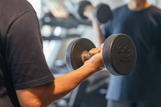 Man gripping dumbbell during workout session in modern gym with training partner nearby, representing social fitness, strength building, muscle recovery and healthy active lifestyle wellbeing