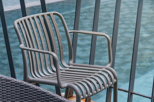 Empty metal chair beside poolside railing overlooking water, representing tranquil digital detox retreat, mindful relaxation and screen-free analog leisure space for wellness getaway lifestyle
