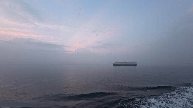 Cinematic real-time video of majestic crepuscular rays behind a massive car carrier ship