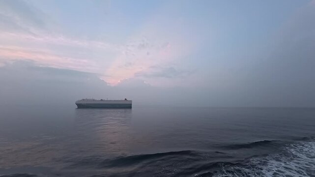 Cinematic real-time video of a large car carrier vessel centered on the ocean with crepuscular rays