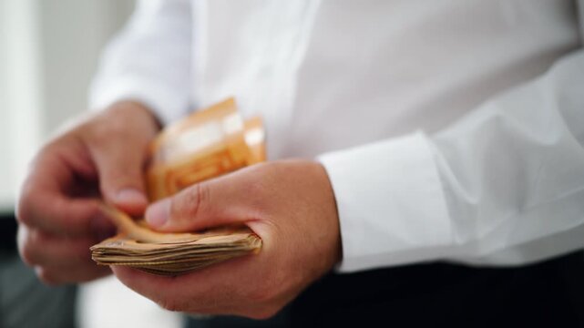 Close-up view of businessman's hands meticulously counting thick wad of fifty euro banknotes, visual metaphor for financial success, profit, savings, and wealth management