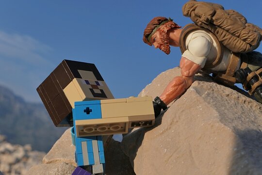 GI JOE action figure of survival instructor Outback, Classified series, helping figure of Minecraft Steve to climb on coastal rock in Croatia. Summer clear blue skies. 