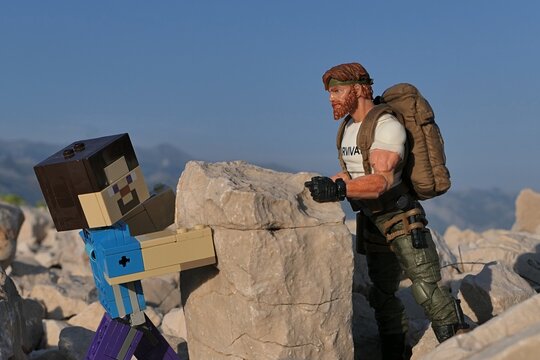 Figures Minecraft Steve and GI JOE Classified edtition survival instructor Outback placing large square block on on Croatian beach, summer daylight sunshine. 