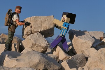 Obraz premium Action figures Minecraft game hero Steve and GI JOE Classified edtition survival instructor Outback placing large square block on on Croatian beach, summer daylight sunshine. 