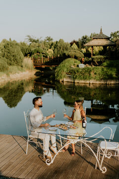 Couple enjoys meal by lake with wine in outdoor setting during golden hour