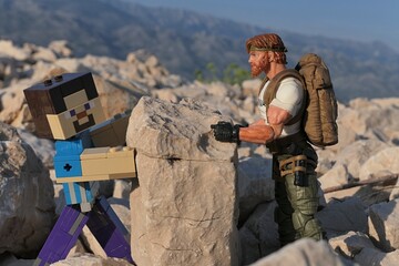 Obraz premium Action figures of Minecraft game hero Steve and GI JOE Classified edtition survival instructor Outback placing large square block on Croatian beach, summer daylight sunshine. 