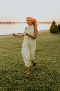Woman runs along riverbank during sunset wearing yellow dress