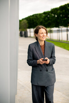 Woman stands outdoors and looks at her phone near the river in the afternoon