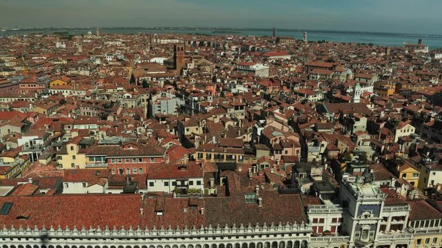 Historic terracotta rooftops and an ancient clock tower overlook the Venetian lagoon under a clear sky. A stunning urban landscape inspiring luxury travel and romantic European escapes.