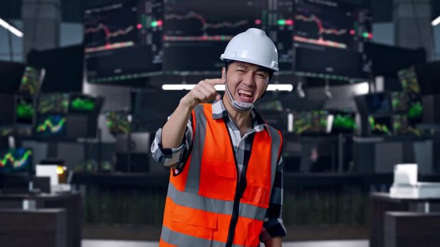 Angry Asian Male Engineer With Safety Helmet Shouting At Someone While Standing at Financial Trading Control Room