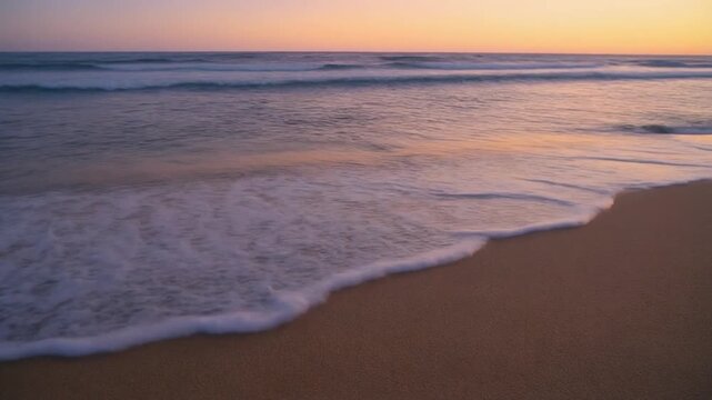 Ocean waves gently lap a sandy beach during a tranquil sunset with soft golden light casting long shadows